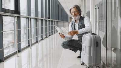 man in black and white blazer sitting beside gray luggage bag