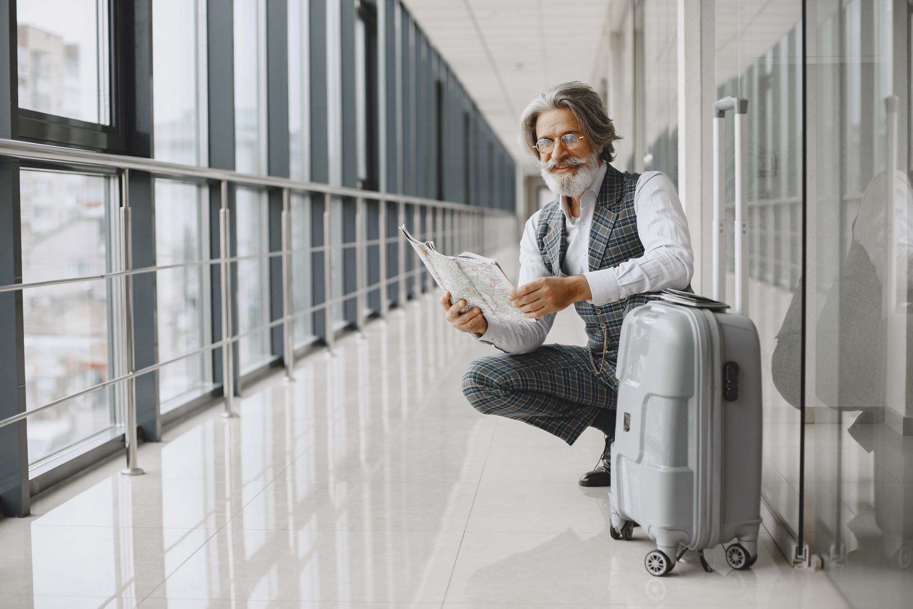 man in black and white blazer sitting beside gray luggage bag