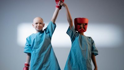 young boys in hospital gowns wearing protective head hear and boxing gloves