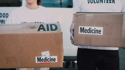 persons wearing volunteer shirts holding cardboard boxes with medicine labels
