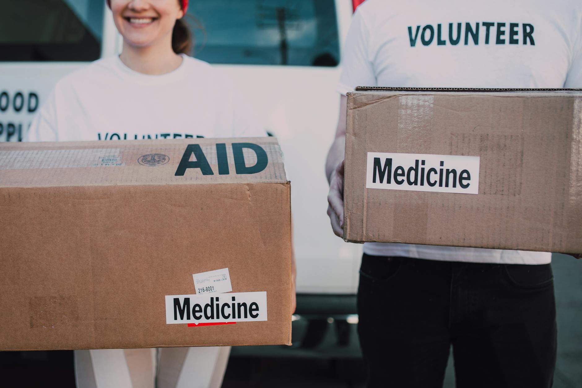 persons wearing volunteer shirts holding cardboard boxes with medicine labels
