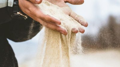 man pouring small pieces of sand on coat