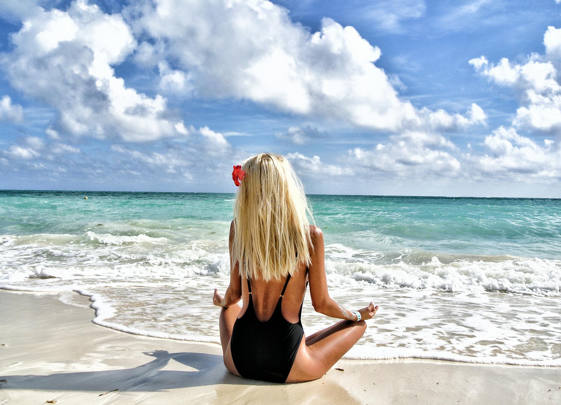 woman wearing black monokini meditating on in front of sea under blue and white sky