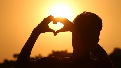 silhouette photo of man doing heart sign during golden hour