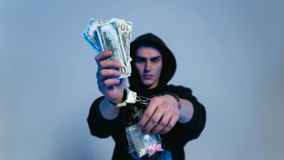 a man in black hoodie sweater wearing handcuffs while holding money and drugs