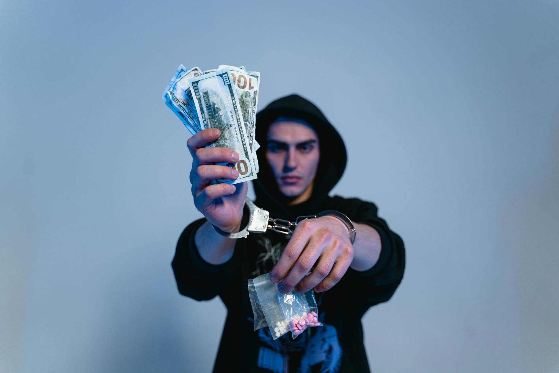 a man in black hoodie sweater wearing handcuffs while holding money and drugs