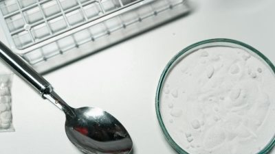 close up shot of silver spoon and illegal drugs on white surface