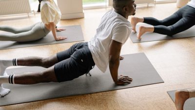 man in white t shirt and black shorts doing stretching on floor