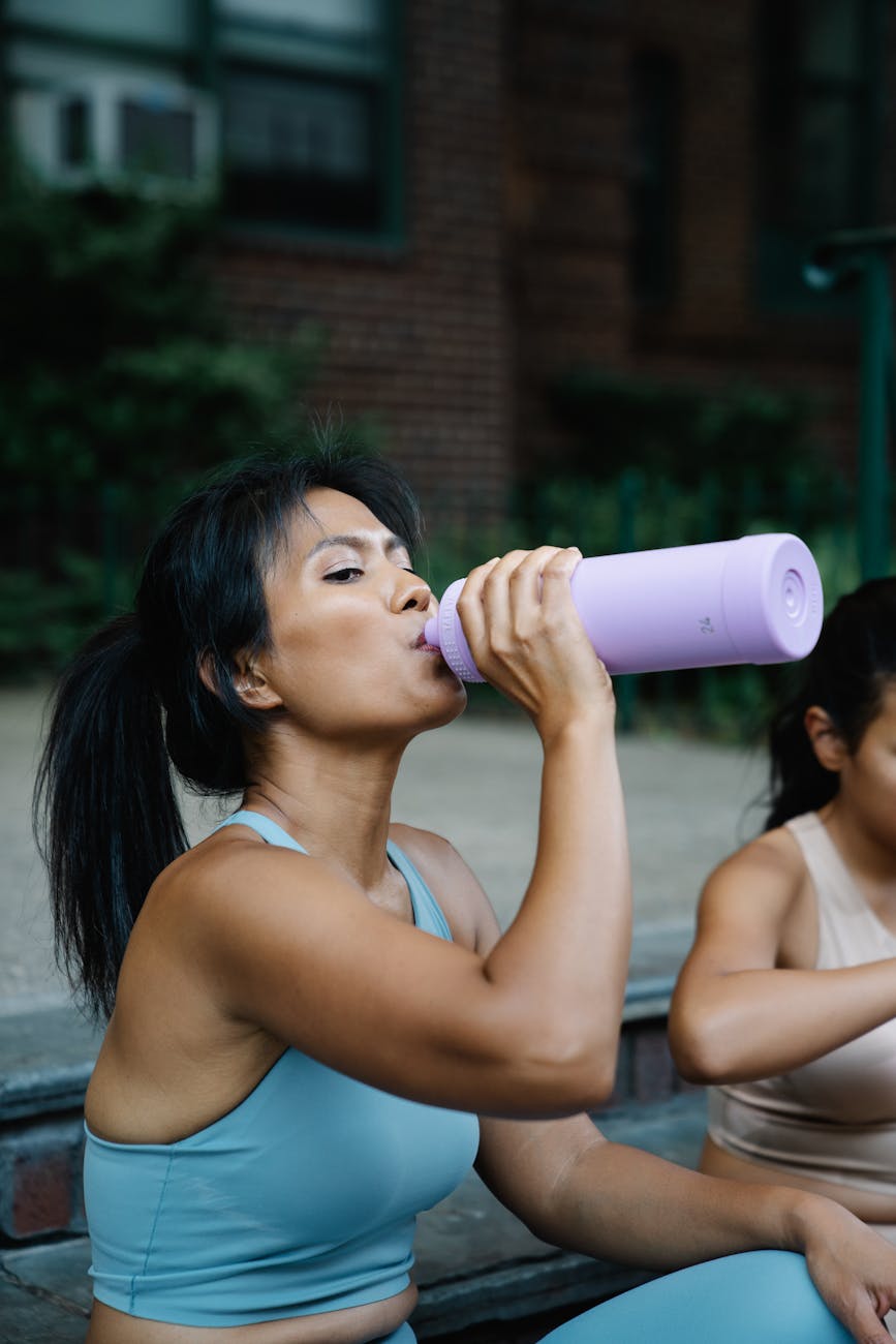woman in blue sports bra drinking from a water bottle
