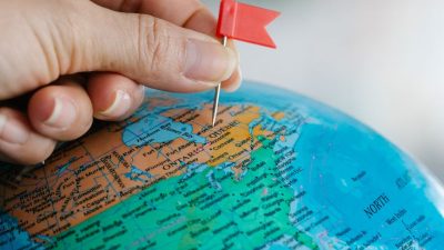 hand holding a tiny red flag near the world globe