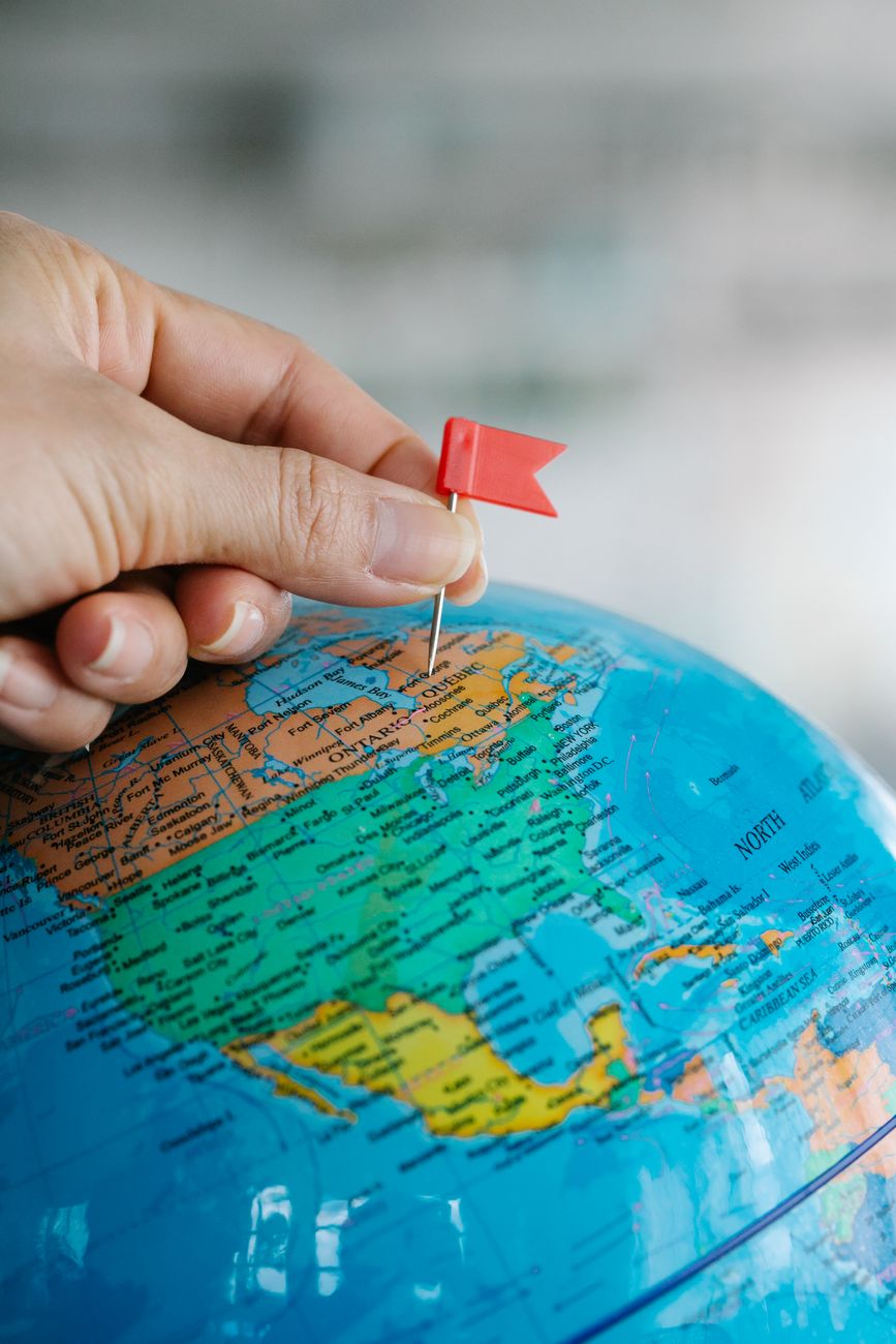 hand holding a tiny red flag near the world globe