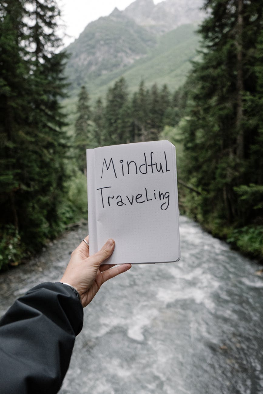 a person holding a book in a forest with a river