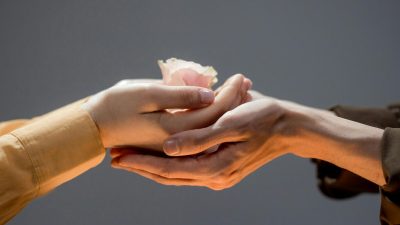 close up of man and woman touching hands and woman holding a rose flower head